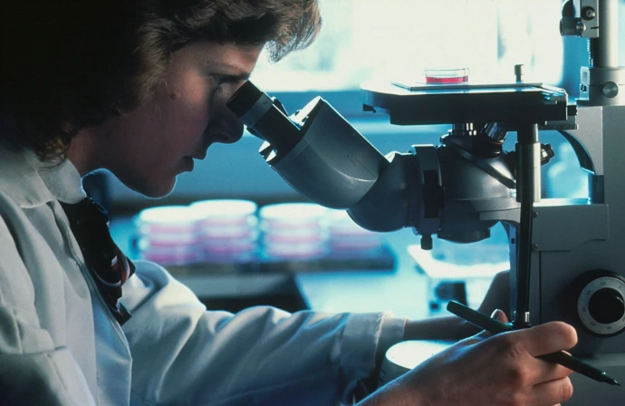 A person in a white lab coat looking through a microscope in a laboratory